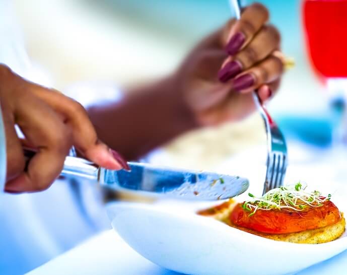 Woman eating sprouts, tomato, and crostini with a fork and knife