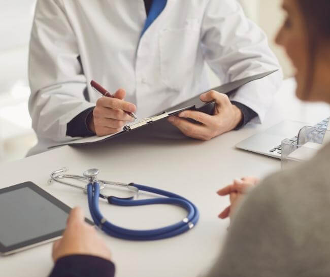 Doctor in white coat writing on clipboard while talking to patient