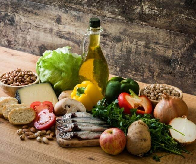 Mediterranean diet foods on a wooden table, including: vegetables, fruits, nuts, fish, and olive oil