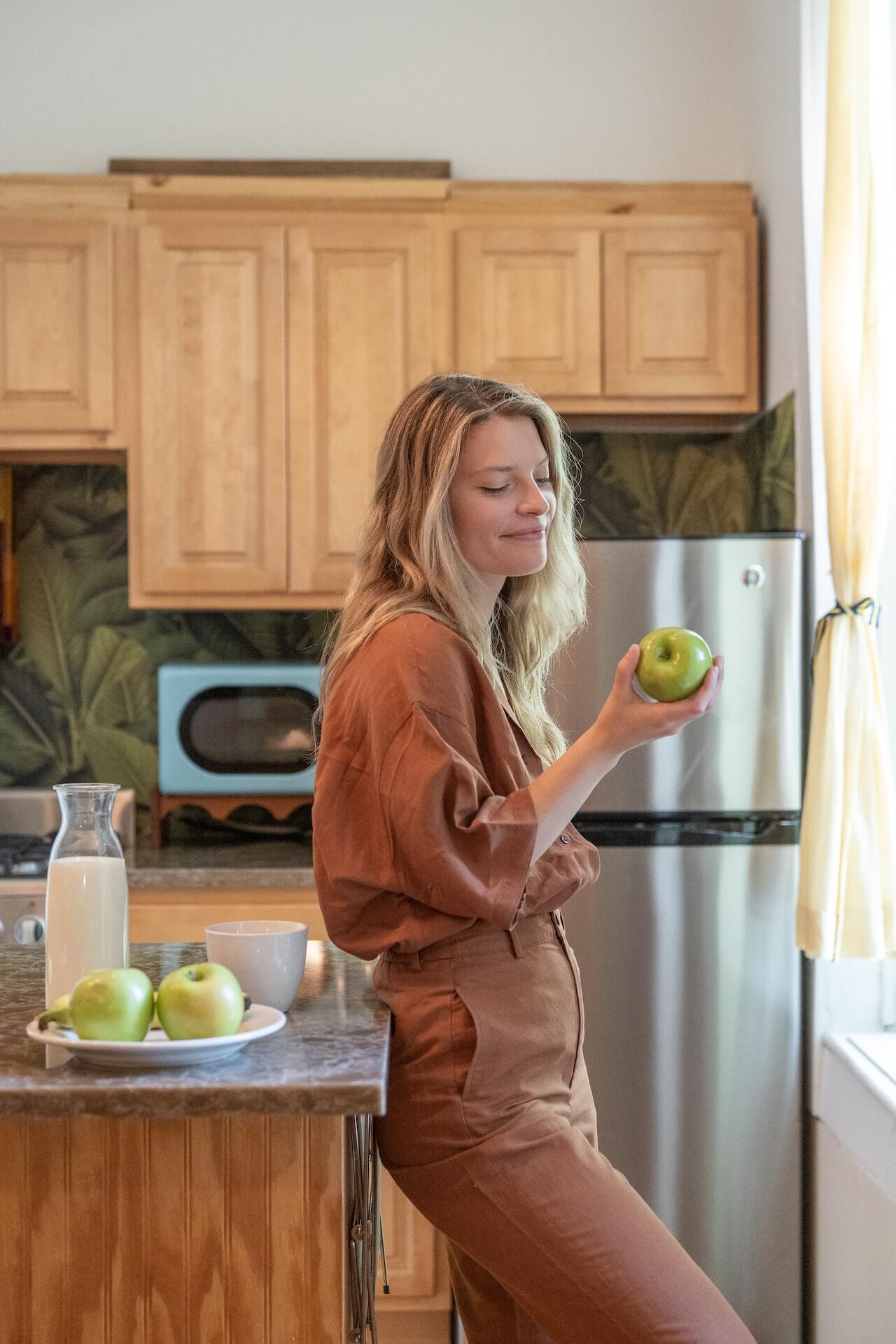 Smiling-woman-leaning-against-the-kitchen-counter-eating-an-apple