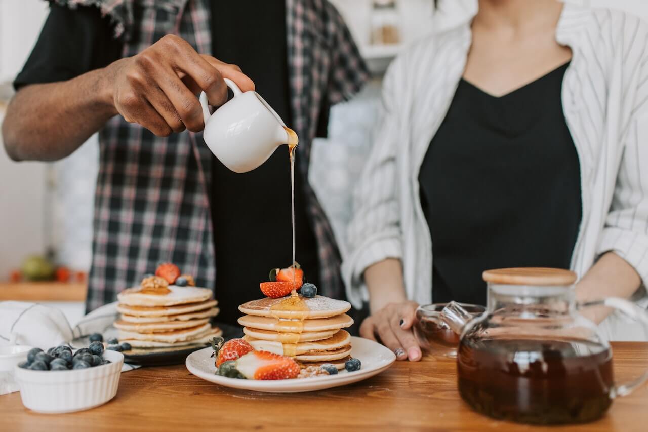 couple-at-home-puring-maple-syrup-to-pancakes