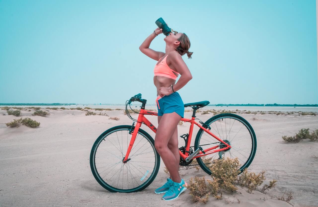 Woman drinking water while standing next to her bike