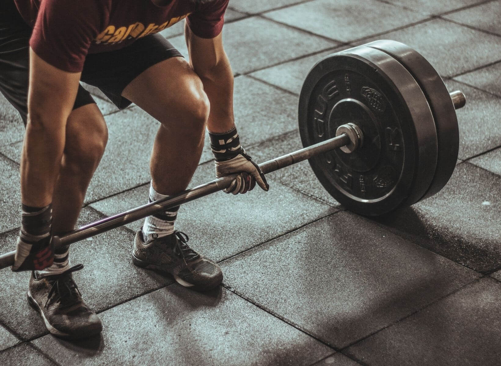 A man bending down to pick up a barbell, a weightlifting exercise that burns calories