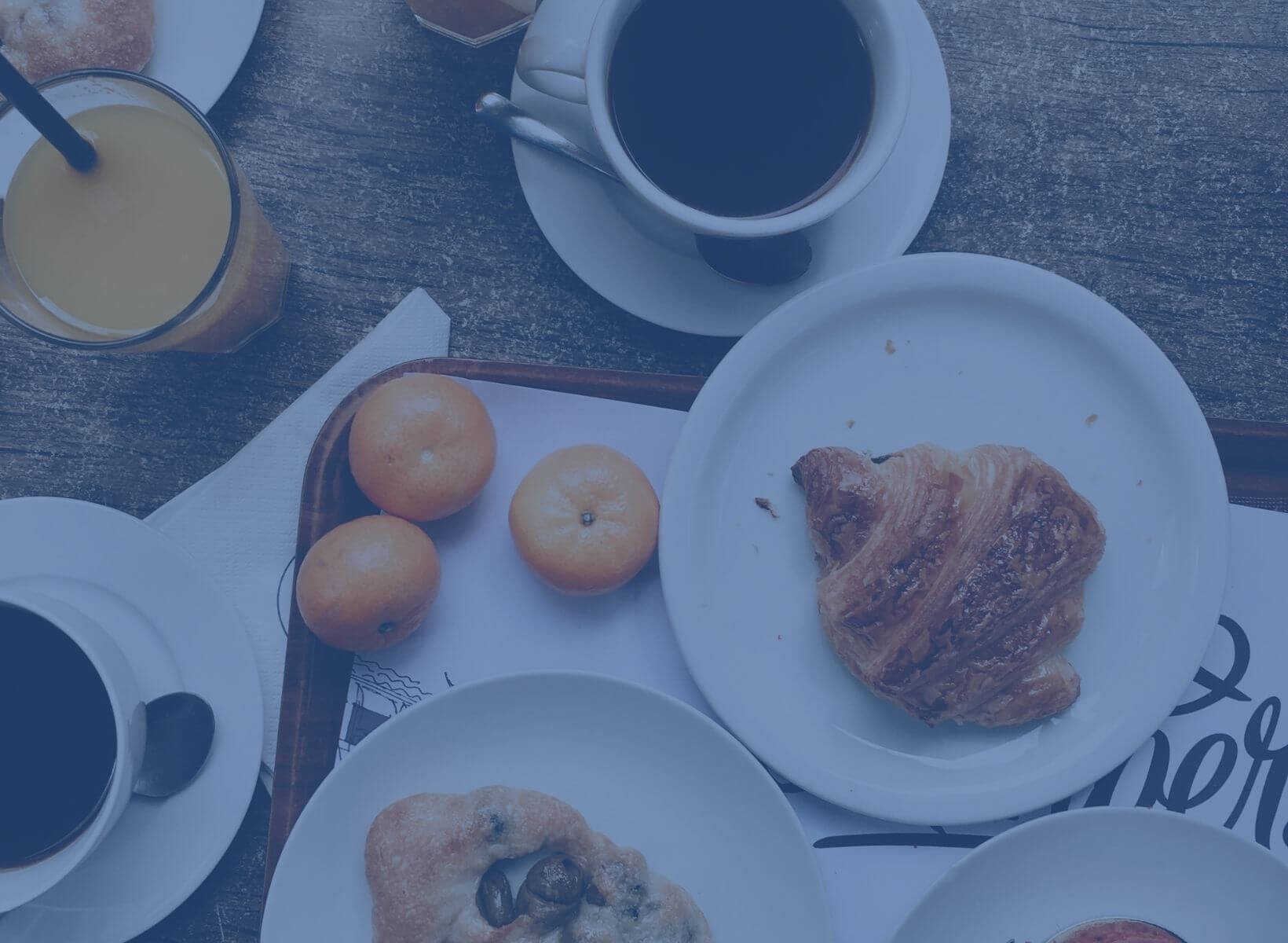 Breakfast pastries on white plates next to glasses of orange juice, oranges and cups of coffee. The sugar in these foods can spike glucose, causing the quick release of insulin.|