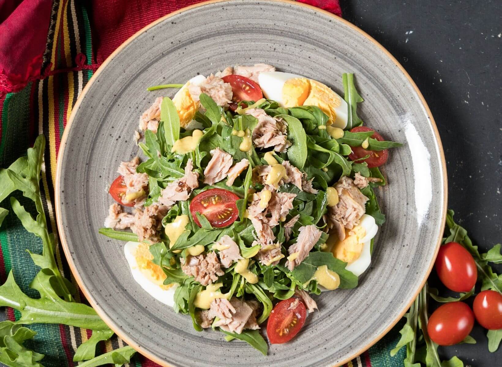 close up of a white plate with a salad made of arugula, lettuce, cherry tomatoes, tuna, and hard boiled eggs