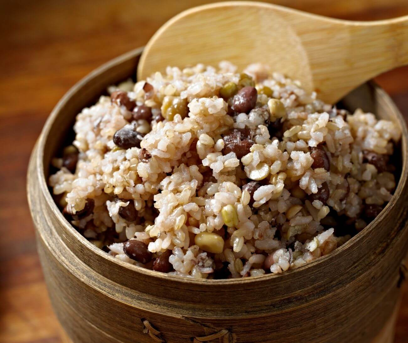 A bowl of brown rice and lentils being served with a wooden spoon