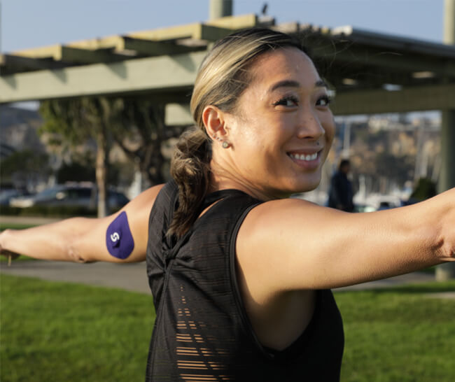 Woman—with outstretched arms—wearing a CGM plus Signos sport cover on her left tricep