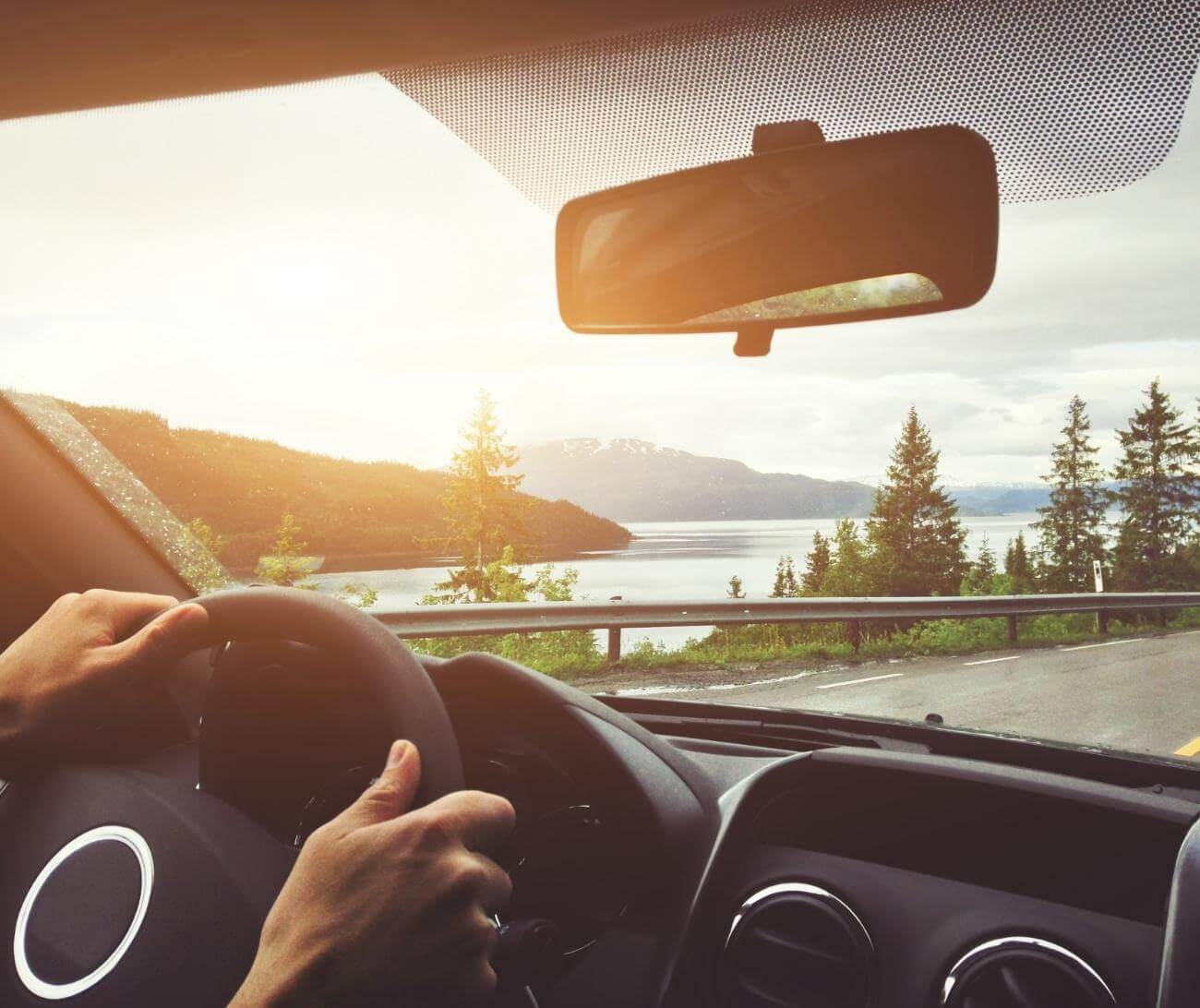 Person driving in car with a scenic view of mountains, trees, and the ocean