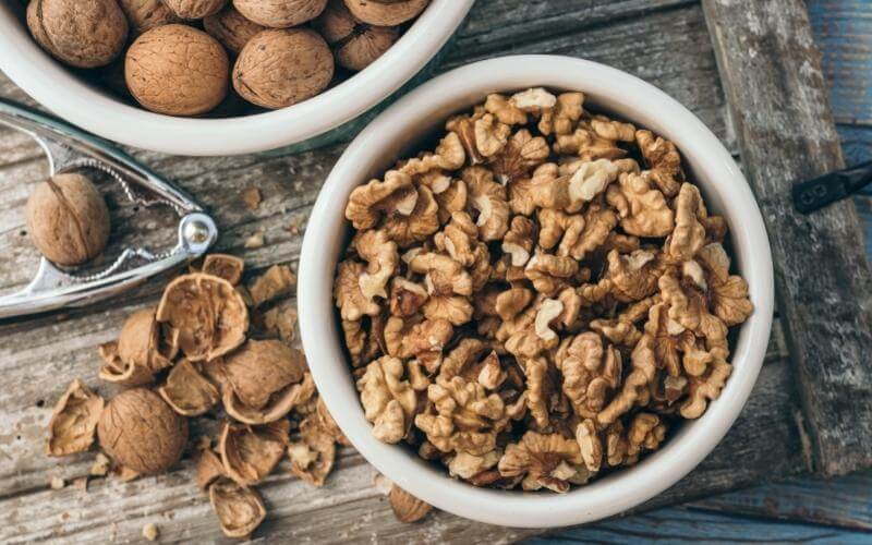 Bowl of cracked walnuts on a table with walnut shells and a nut cracker sitting next to it