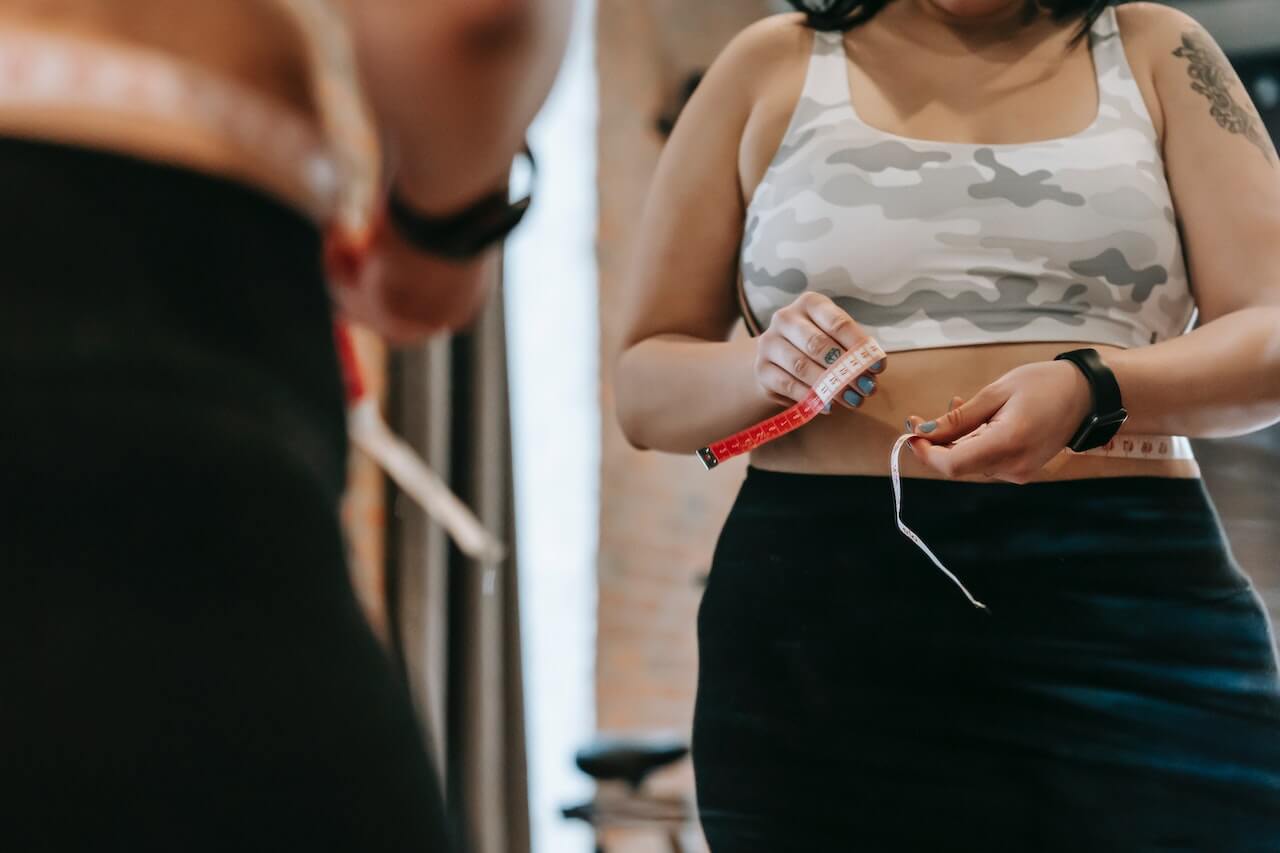 woman-measuring-waist-with-tape-in-gym