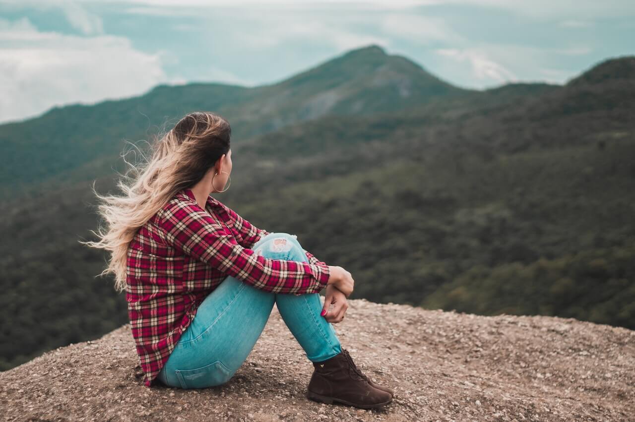 Woman-Sitting-on-Ground-Overlooking-a-Hill