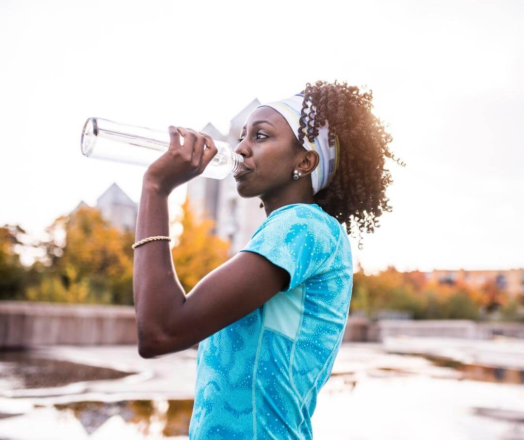 woman in workout clothes drinking water from a reusable bottle