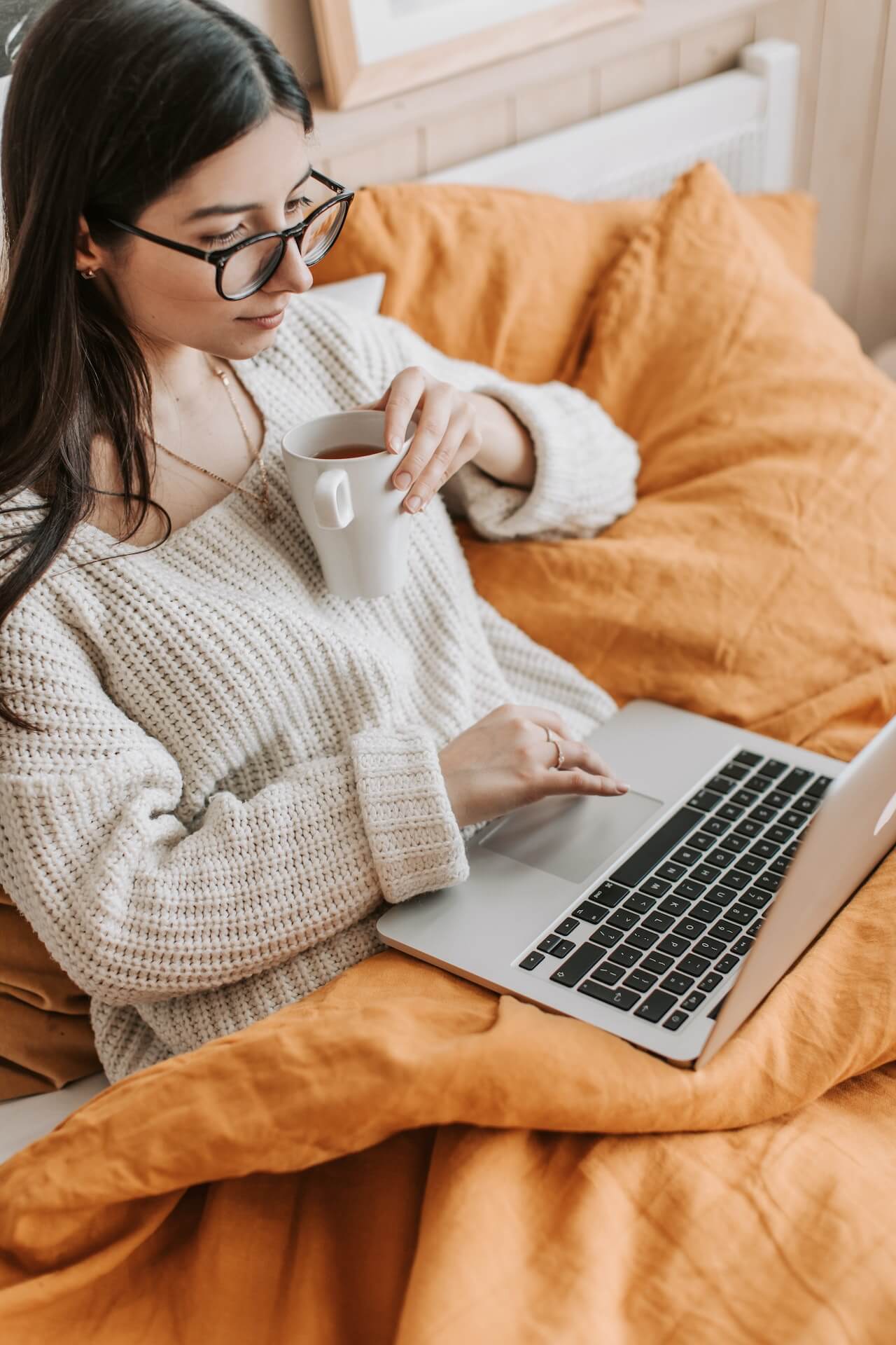 Young-woman-using-laptop-and-drinking-tea-on-bed