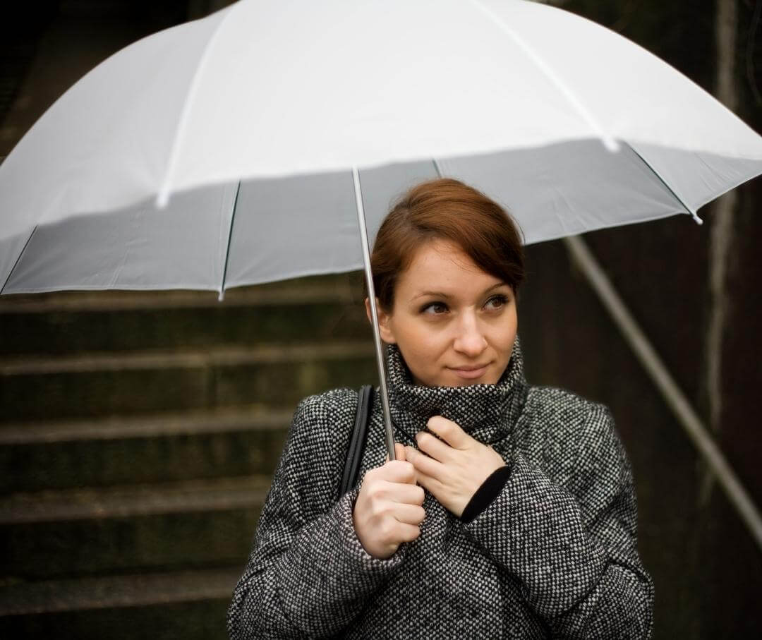 Woman in a jacket outdoors standing under a white umbrella