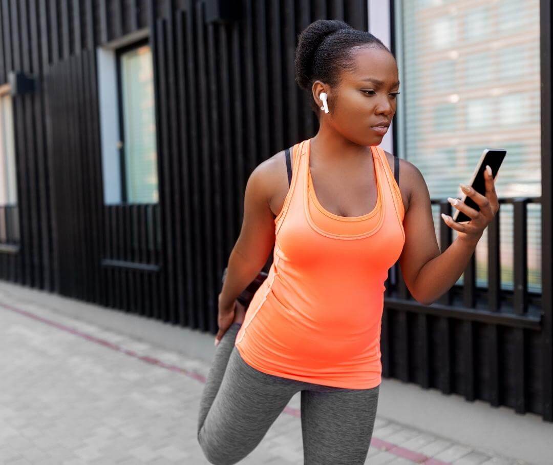 woman in workout clothes stretching and looking at her smartphone