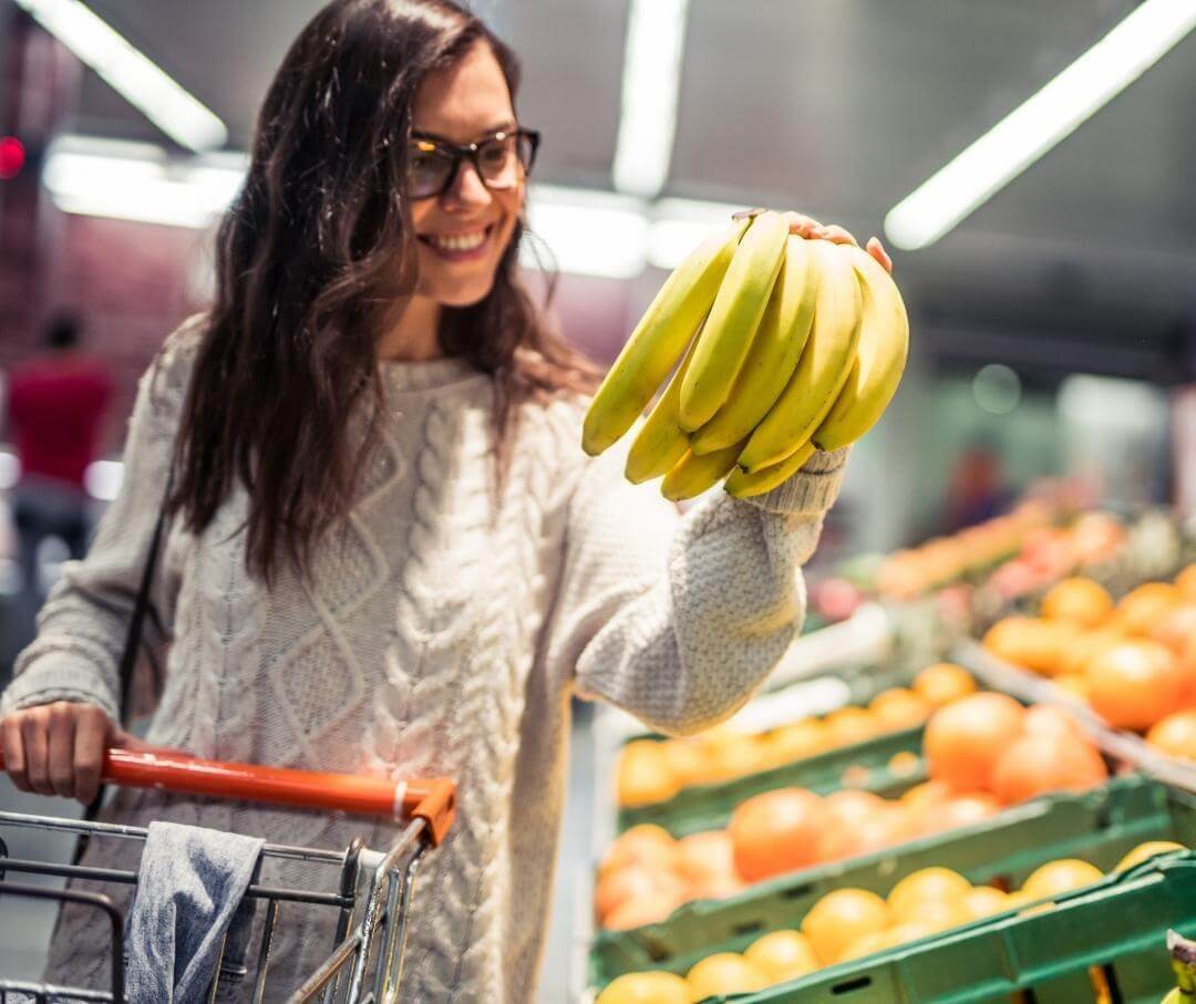 Woman holding a bunch of bananas in the produce section of a grocery store