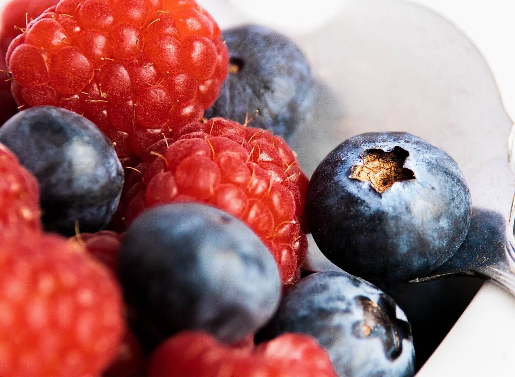 Close up shot of raspberries and blueberries in a bowl with a spoon