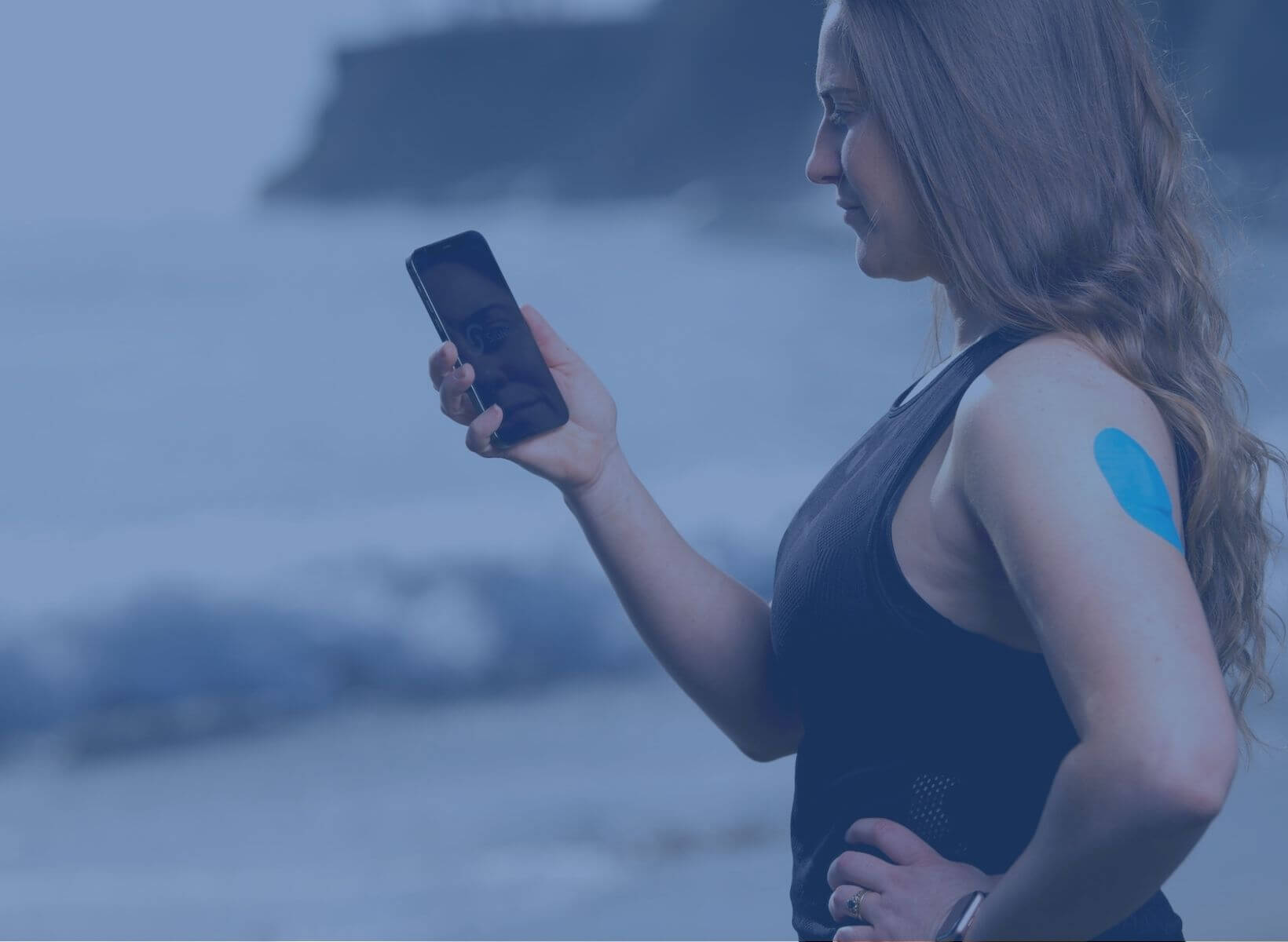 woman wearing a continuous glucose monitor holding a smart phone and looking at it