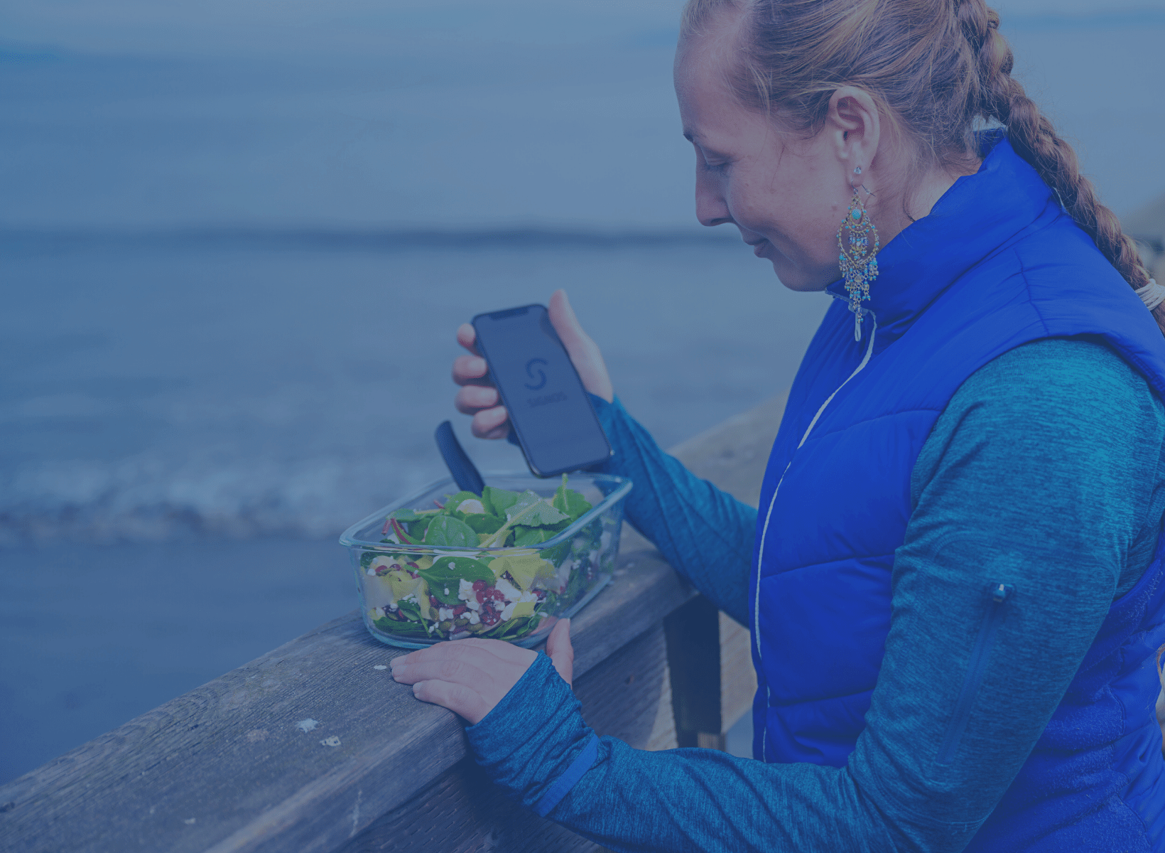 Woman holding an iPhone for counting calories in the salad she will eat.