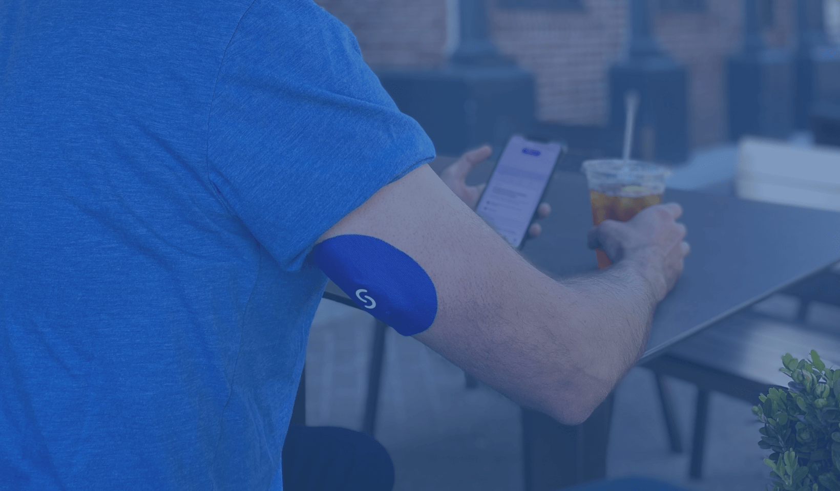 A man sitting at a table with his elbow resting on a table. He has a CGM with a sport cover on his arm.